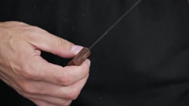 Bir adamın el yapımı, el yapımı, yıpranmış çelik bir bıçakla ahşap bir sapı olan ilkel bir el resmi. Bu rustik alet hayatta kalma, tehlike ve klasik zanaat temalarını çağrıştırıyor..