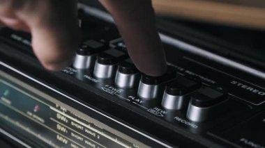 Arkadaki siyah plastik tuşları, gümüş detayları ve radyo ayarlayıcısını gösteren klasik bir kaset kaydedicinin açılı, yüzeysel odaklı görüntüsü 80 'li yılların modasını çağrıştırıyor..