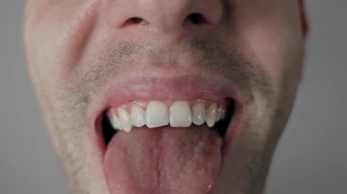 Sakallı, komik suratlar yapan, dilini dışarı çıkaran, yuvarlayan ve alışılmadık şekillerde katlayan bir adamın makro görüntüsü. Çarpık dişlerini şapşal, eğlenceli ve komik bir ifadeyle gösteriyor..