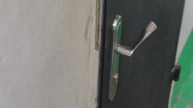 Yakın çekim yavaş yavaş eski, gümüş renkli bir kapı kolunun üzerinden geçerek çatlak bir duvarın yanındaki eskimiş bir kapının üzerinde yaş ve gizem hissi yaratıyor..