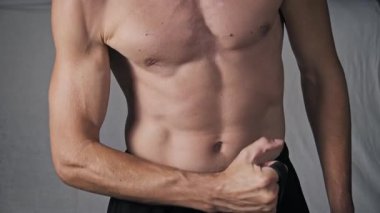 Gövdesi tanımlı atletik bir adamın, siyah direniş bandını kullanarak bisepsi kıvırırken, kas tanımı yaparken yakın plan çekimleri..