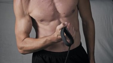 İyi tanımlanmış fiziği olan bir adam kol egzersizi için kauçuk genişletici kullanır. Video, göğüs ve karın kaslarının direnç egzersizi sırasında kapalı alanda kasıldığını gösteriyor..
