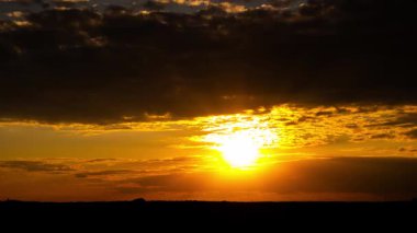 Geniş açılı zaman çizelgesi, şiddetli, karanlık fırtına bulutlarının ardında parlak bir güneşin batışını gösteriyor. Gökyüzü turuncuya dönerken siluetli bir manzara ufkunun üzerine dramatik altın güneş ışınları saçıyor..
