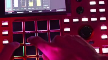 Kırmızı elektronik davul makinesinin parlayan pedlerine aktif olarak basan bir elin yakın çekim görüntüsü ekranındaki görsel geribildirim ile ritimler yaratıyor..