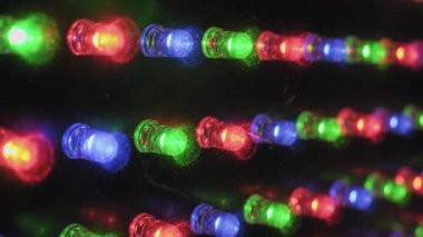 Bir panel üzerinde bireysel RGB LED diyotlarının aşırı yakın plan çekimleri, kırmızı, yeşil ve mavi ışıkların tozlu bir yüzey üzerinde çeşitli desenlerde titreşmesi, canlı bir teknoloji görüntüsü yaratıyor.