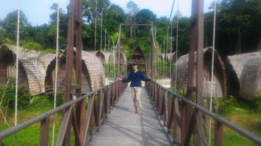 Kalimantan 'dan geleneksel bir evin arka planına karşı ahşaptan yapılmış yaya köprüsünde duran bir adam.