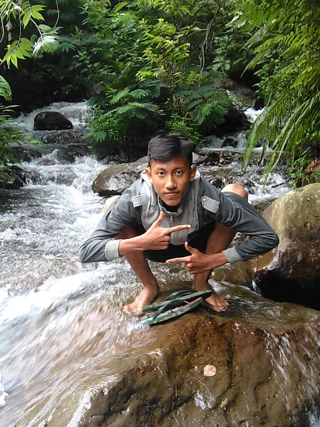 インドネシア中部ジャワ州サランガンで休暇中に清く新鮮な川の流れを持つ岩の上にポーズをとる男の表現 — ストック写真