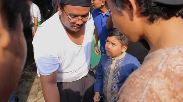 Jakarta, Endonezya - 08 11 2019: Çocuk beyaz giyinmiş sırıtan bir adama kurbanlık hayvanını teslim ediyor.