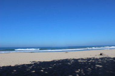 Gökyüzünün arka planı parlak mavi çizgilerle ve kıyı küçük dalgalarla tamamlanmış.