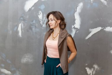 Fashionable and stylish girl posing in green culottes, blouse and sweater against a gray wall