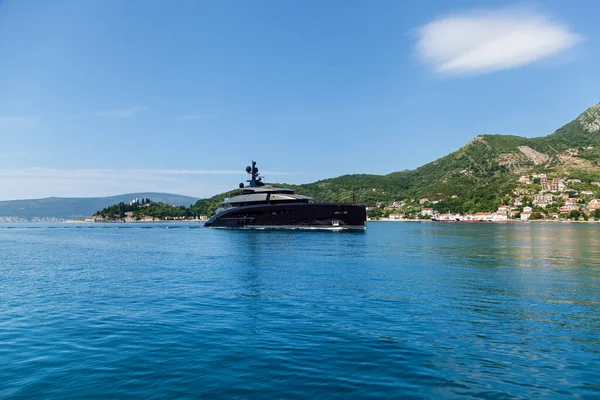 A large black motor yacht is sailing on the water near the shore