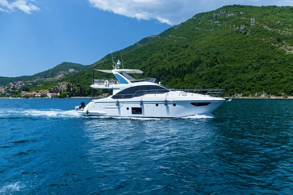 A large white motor yacht is sailing on the water near the shore