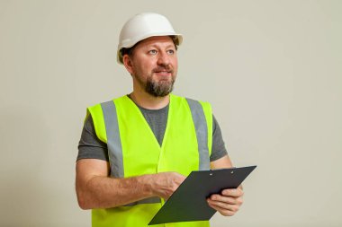 Yelek ve beyaz miğfer takmış bir erkek işçi beyaz bir arka planda kağıt sayfaları için şarjör içeren bir klasör tutuyor..