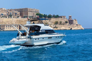 Büyük beyaz bir motor yatı kıyıya yakın sularda yüzüyor.