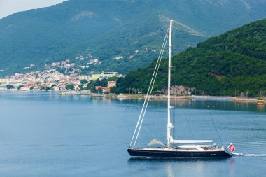 Büyük siyah bir yelkenli yat sahil boyunca süzülüyor.