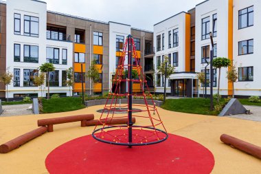 Çeşitli çalılıkları ve ağaçları olan yeşil dinlenme alanı, çok katlı bir binanın bahçesinde bir çocuk parkı.