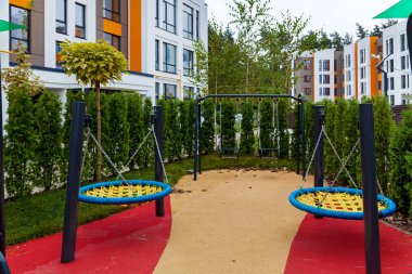 Çeşitli çalılıkları ve ağaçları olan yeşil dinlenme alanı, çok katlı bir binanın bahçesinde bir çocuk parkı.