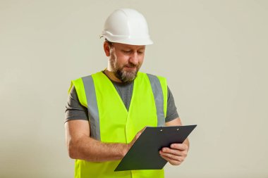 Yelek ve beyaz miğfer takmış bir erkek işçi beyaz arka planda bir kağıt için ataç içeren bir klasör tutuyor..