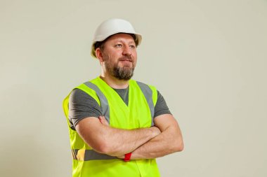 Çelik yelek ve farklı pozlarda beyaz miğfer giyen bir işçi beyaz arka planda duruyor.