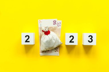 2023 numaralı ahşap beyaz küpler ve sarı arka planda bir çanta dolusu hediye ya da bozuk para. Zengin ve mutlu bir Noel ve yeni yıl konsepti.