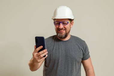 Beyaz miğferli, gözlüklü, gri tişörtlü bir adam telefonda konuşuyor.