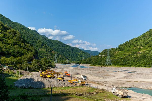 Очистка русла реки в горах, строительная техника, экскаваторы и грузовики устраняют последствия весенних паводков горных рек.