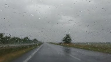 Arabanın ön camına yağmur damlaları yaklaşan rüzgardan yükselir. Yağmurda yolculuk.