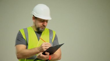 Yelek ve beyaz miğfer takmış bir erkek işçi beyaz arka planda bir kağıt için ataç içeren bir klasör tutuyor...