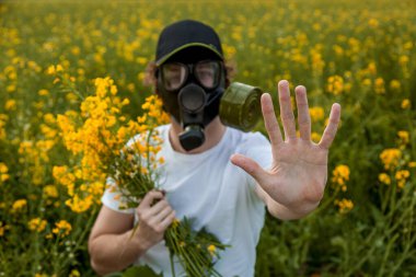 Sarı kolza tohumu çiçekleriyle dolu bir arazide gaz maskeli genç bir adam..