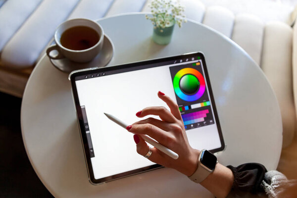 A girl in a cafe draws with a stylus on a graphics tablet.Remote work of a designer, visualizer or artist
