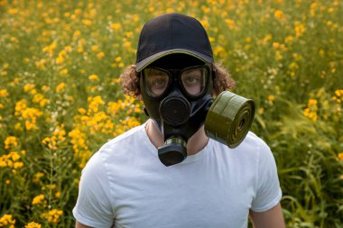 Sarı kolza tohumu çiçekleriyle dolu bir arazide gaz maskeli genç bir adam..