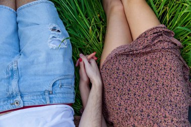 Adam ve kız yeşil çimenlerde uzanmış el ele tutuşuyorlar.