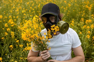 Sarı kolza tohumu çiçekleriyle dolu bir arazide gaz maskeli genç bir adam..