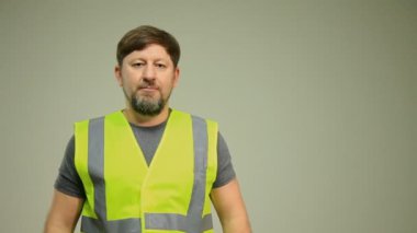 Güvenlik kaskı ve yüksek görüş açısına sahip yelek giyen bir inşaat işçisi arka planda dijital tablet kullanır. Görüntü, teknolojinin modern inşaat çalışmalarına entegrasyonunu vurguluyor, güvenlik ve verimliliği vurguluyor.