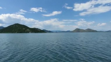 Parlak mavi bir gökyüzünün altında yemyeşil dağlarla çevrili sakin bir göle sahip huzurlu bir manzara. Berrak sular doğal güzelliği yansıtıyor, huzurlu ve rahatlatıcı bir atmosfer yaratıyor doğa severler ve açık hava meraklıları için mükemmel..