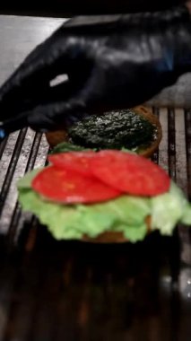 Adım adım hamburger montajı: sulu dana köftesi, erimiş çedar, taze marul, domates ve kızarmış ekmeğin üzerine aromalı yeşil sos. Hamburgerciler için ağız sulandırıcı bir lezzet