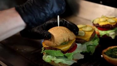 Siyah eldivenli bir şef lezzetli köfteli, işlenmiş peynirli, taze sebzeli ve otlu iştah açıcı bir hamburger yapar. Fast food ve restoran reklamları için ideal..