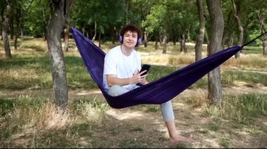 Genç bir adam hamakta dinlenmekten, kulaklıkla müzik dinlemekten hoşlanır. Rahatlama, müzik ve uygun aksesuarların reklamını yapmak için harika bir an..