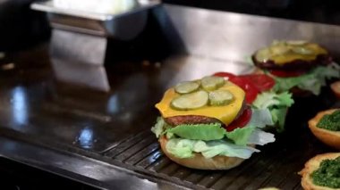 Siyah eldivenli şef et, işlenmiş peynir, taze salatalık ve domatesli bir burger yapıyor. Fast food restoranları, reklamlar ve yemek blogları için mükemmel bir video..