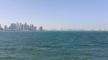 Kıyı şeridi boyunca yükselen yüksek gökdelenleri olan modern bir kıyı şehrinin panoramik manzarası, parlak mavi bir gökyüzüne ve berrak bir turkuaz denize karşı.