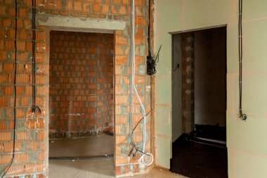 Tamamlanmamış konut alanları, kaba tuğla döşeme, elektrik kabloları ve sıva olmayan kapılar, apartman yenileme veya inşaatın ham aşamasını yakalıyor.