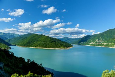 Sarmal turkuaz bir nehrin panoramik manzarası canlı yeşil orman tepeleri ve parlak mavi gökyüzünün altında dramatik bulutlarla çevrili.