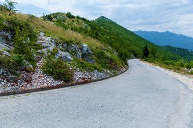 Boş asfalt yol kayalık yamaçlar ve bulutlu gökyüzü ile bereketli dağ manzarası boyunca kıvrımlı seyahat, macera veya doğa kavramları için mükemmel.