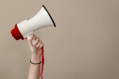 Manikürlü tırnakları olan, beyaz ve kırmızı bir megafon kaldıran, bej arka planda duyuruyu, protestoyu ya da eylemi simgeleyen bir kadın eli.