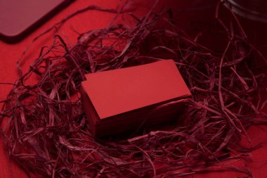 Kırmızı kumaş arka planında dairesel bir kırmızı rafya yuvasına yerleştirilmiş düz kırmızı dikdörtgen kartvizitler, neşeli ve cesur bir markalaşma veya ambalaj kavramını çağrıştırıyor.