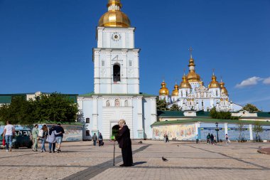 Kyiv 'deki St. Michael' s Altın Kubbe Manastırı. Meydanda yürüyen ziyaretçiler, canlı gökyüzü ve güneş ışığı ikonik mimariyi aydınlatıyor.