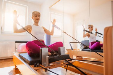 Kadın evinde pilates reformatör yatağında egzersiz yapıyor..