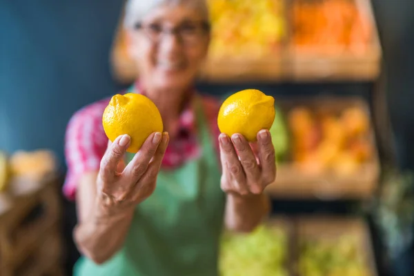 Worker in fruits and vegetables shop is holding lemons. Close up of lemon.