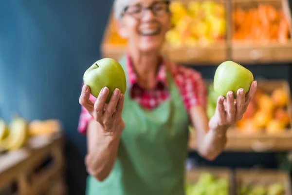 Worker in fruits and vegetables shop is holding apples. Close up of green apples.