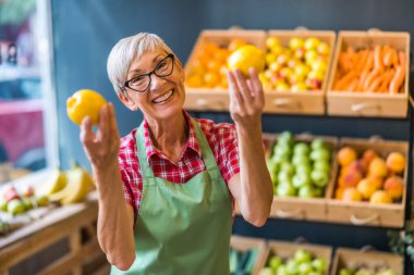 Worker in fruits and vegetables shop is holding lemons.